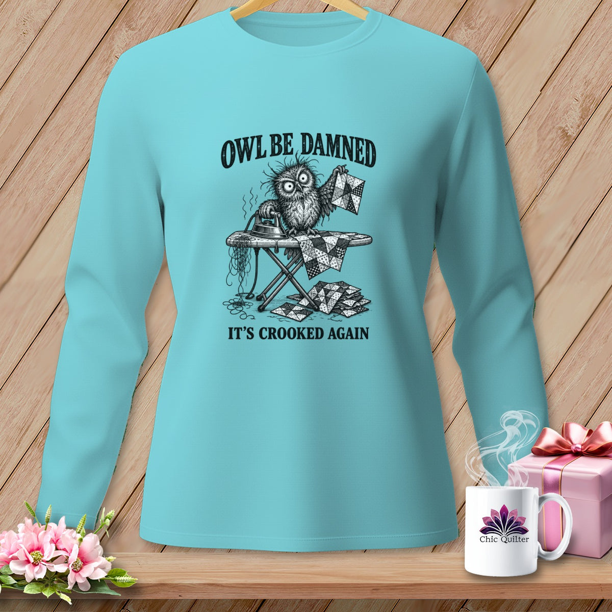 Turquoise long-sleeve shirt with a comical owl ironing a crooked quilt.