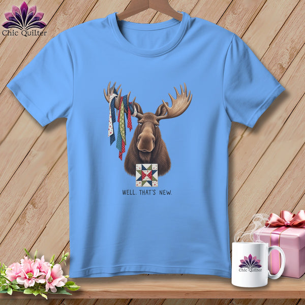 Light blue t-shirt with moose wearing patterned ribbons and quilt square, text "WELL. THAT'S NEW."