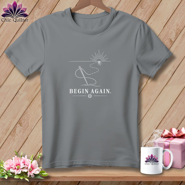 Gray t-shirt with white sewing needle design and text "BEGIN AGAIN."