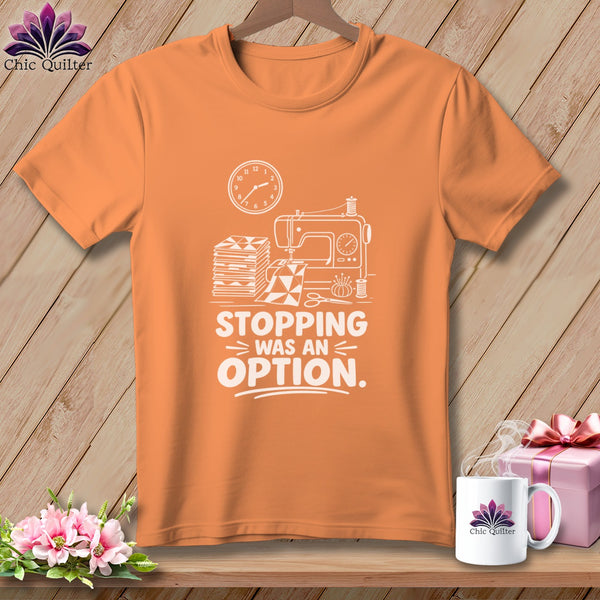 Orange t-shirt with sewing machine, fabric stack, and text "STOPPING WAS AN OPTION."