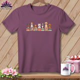 Mauve short-sleeve t-shirt hanging on a wooden wall, featuring a graphic of seven cartoon dogs sitting on stacked quilts.