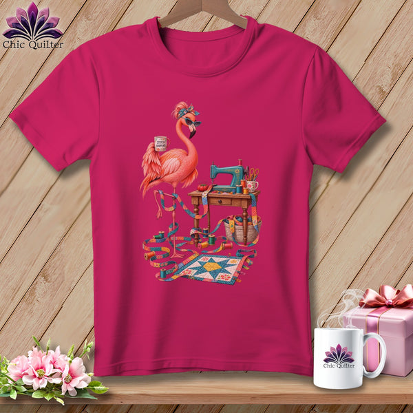 Pink t-shirt with a flamingo at a sewing machine with a quilt and supplies.