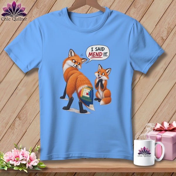 Light blue t-shirt with two cartoon foxes, one with a quilted tail patch, and a speech bubble saying "I SAID MEND IT."