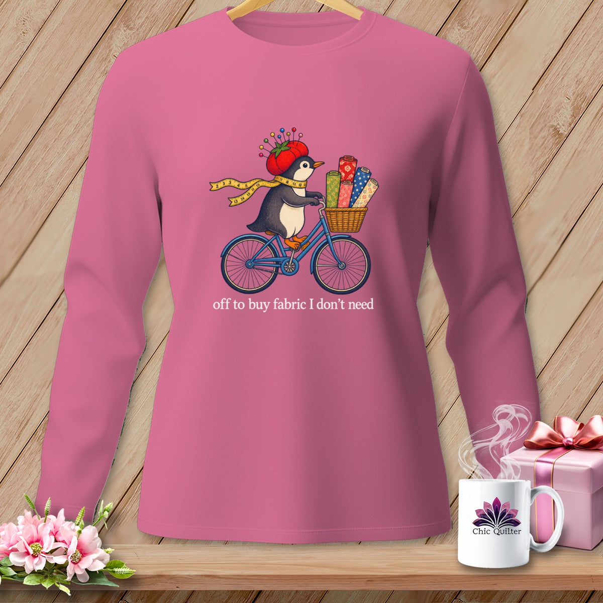 Pink long-sleeve shirt with penguin on bike, carrying fabric, and text "off to buy fabric I don't need".