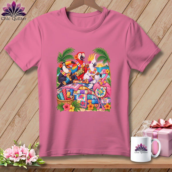 A pink t-shirt displays a graphic of tropical birds playing instruments and quilting on a beach.
