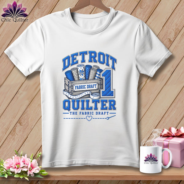 White t-shirt with a blue graphic reading Detroit Quilter featuring fabric bolts in a crate.
