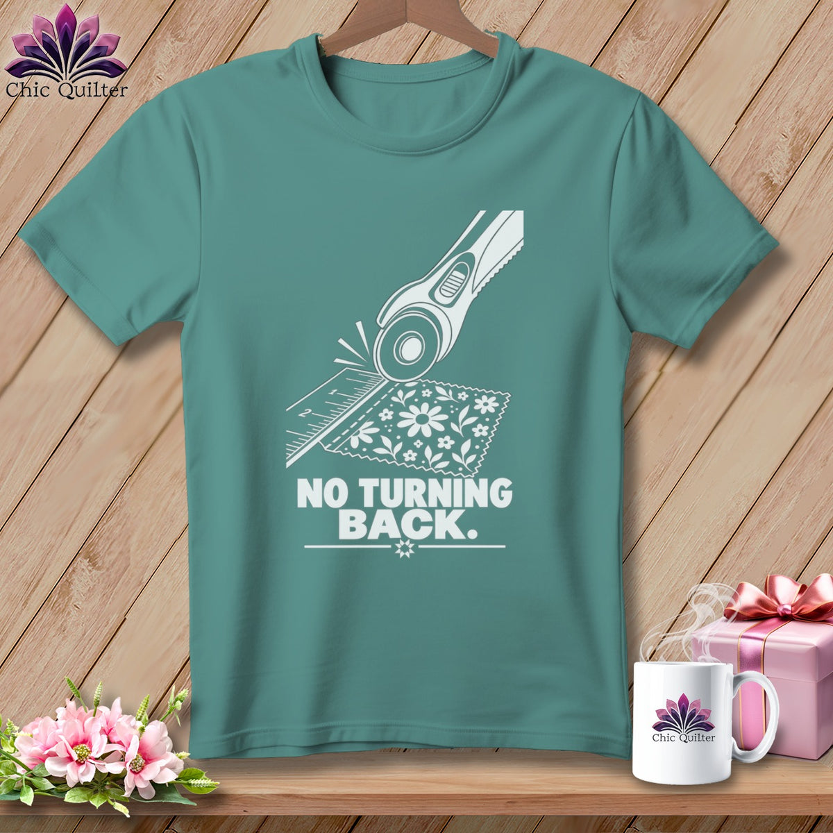 Teal t-shirt with white graphic of rotary cutter, ruler, fabric, and text "NO TURNING BACK."