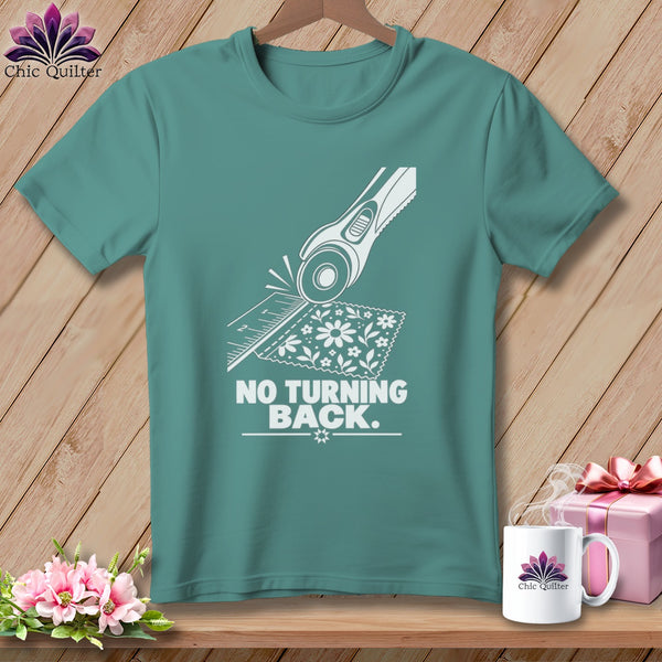 Teal t-shirt with white graphic of rotary cutter, ruler, fabric, and text "NO TURNING BACK."