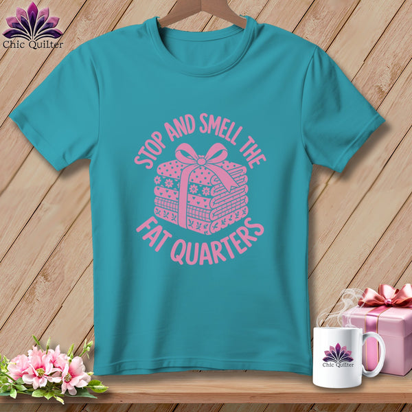 Teal t-shirt featuring pink text that reads Stop and Smell the Fat Quarters and a wrapped stack of fabric.