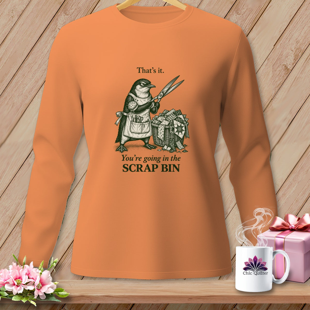 Orange long-sleeve shirt with a penguin holding scissors and a scrap bin, text reads "That's it. You're going in the SCRAP BIN".