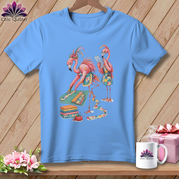 Light blue t-shirt with two flamingos sewing with fabric, rotary cutter, and pins.