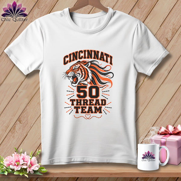 White t-shirt with a roaring tiger design and text reading Cincinnati 50 Thread Team on a wooden surface.