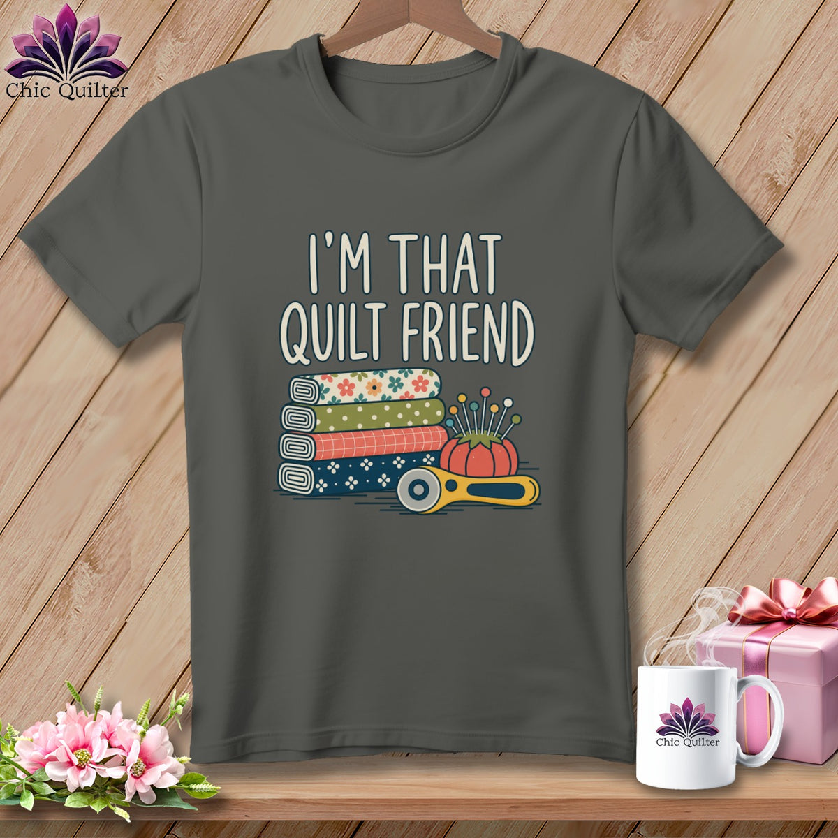 A dark gray t-shirt with the text I'M THAT QUILT FRIEND above stacked fabric, pins, and a rotary cutter.