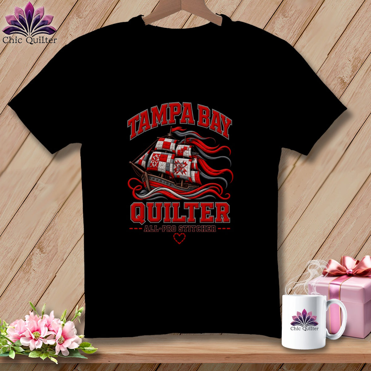 A black t-shirt printed with a graphic featuring a quilt-patterned ship and text reading Tampa Bay Quilter All-Pro Stitcher.
