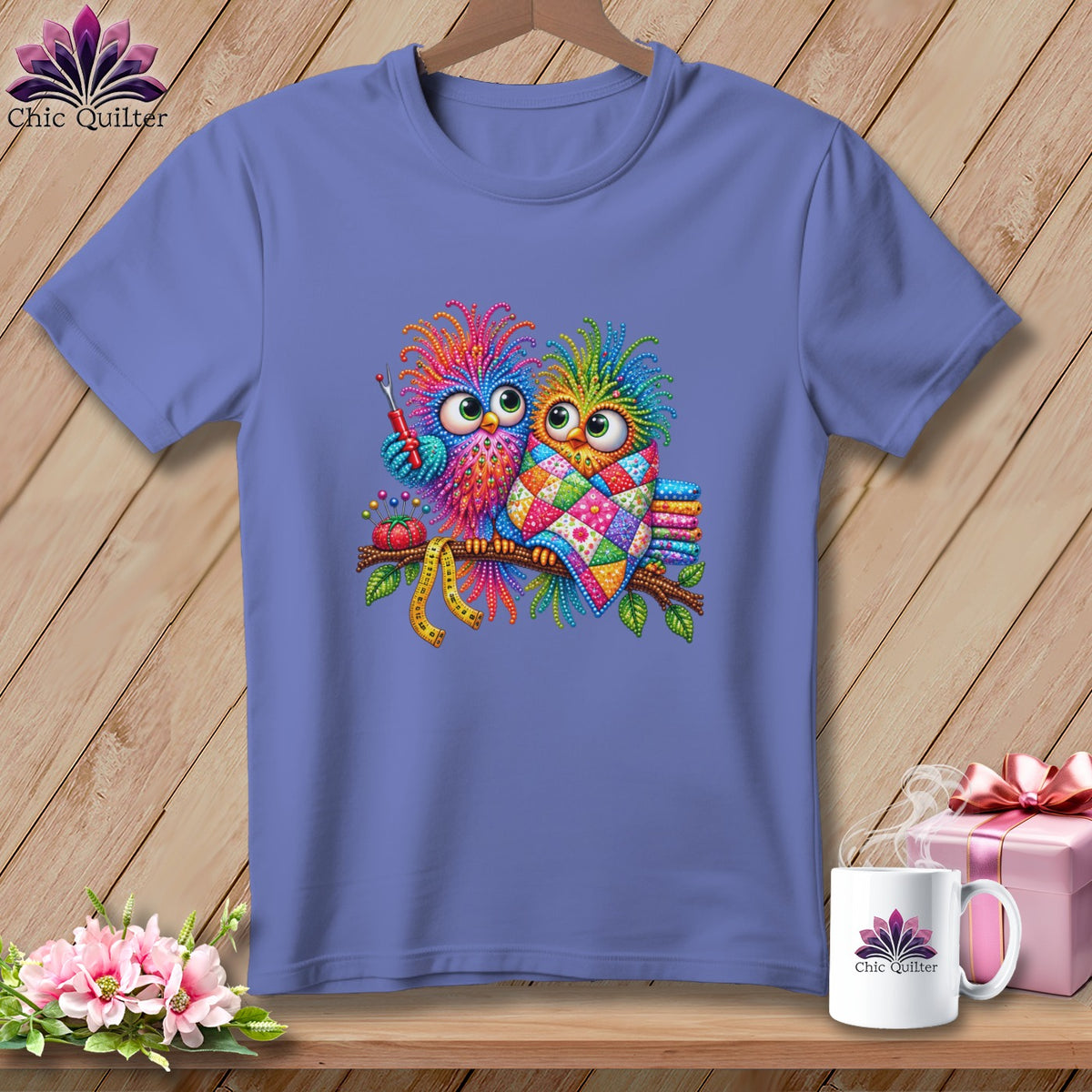 Periwinkle blue t-shirt featuring two colorful cartoon owls on a branch with sewing accessories.